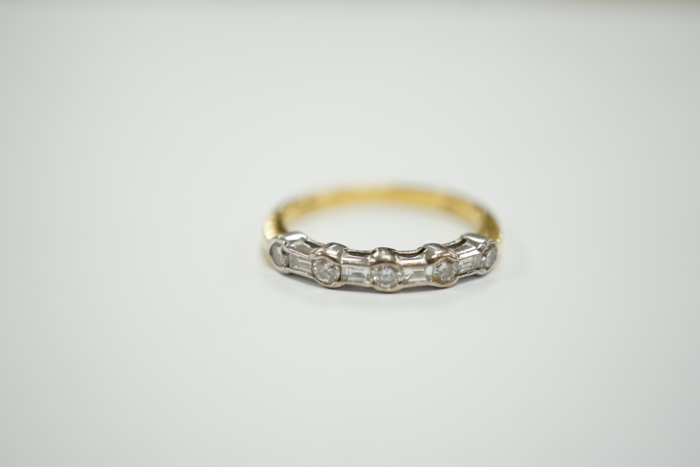 A modern 18ct gold, round and baguette cut diamond set half hoop ring, size N/O, gross weight 3.2 grams.